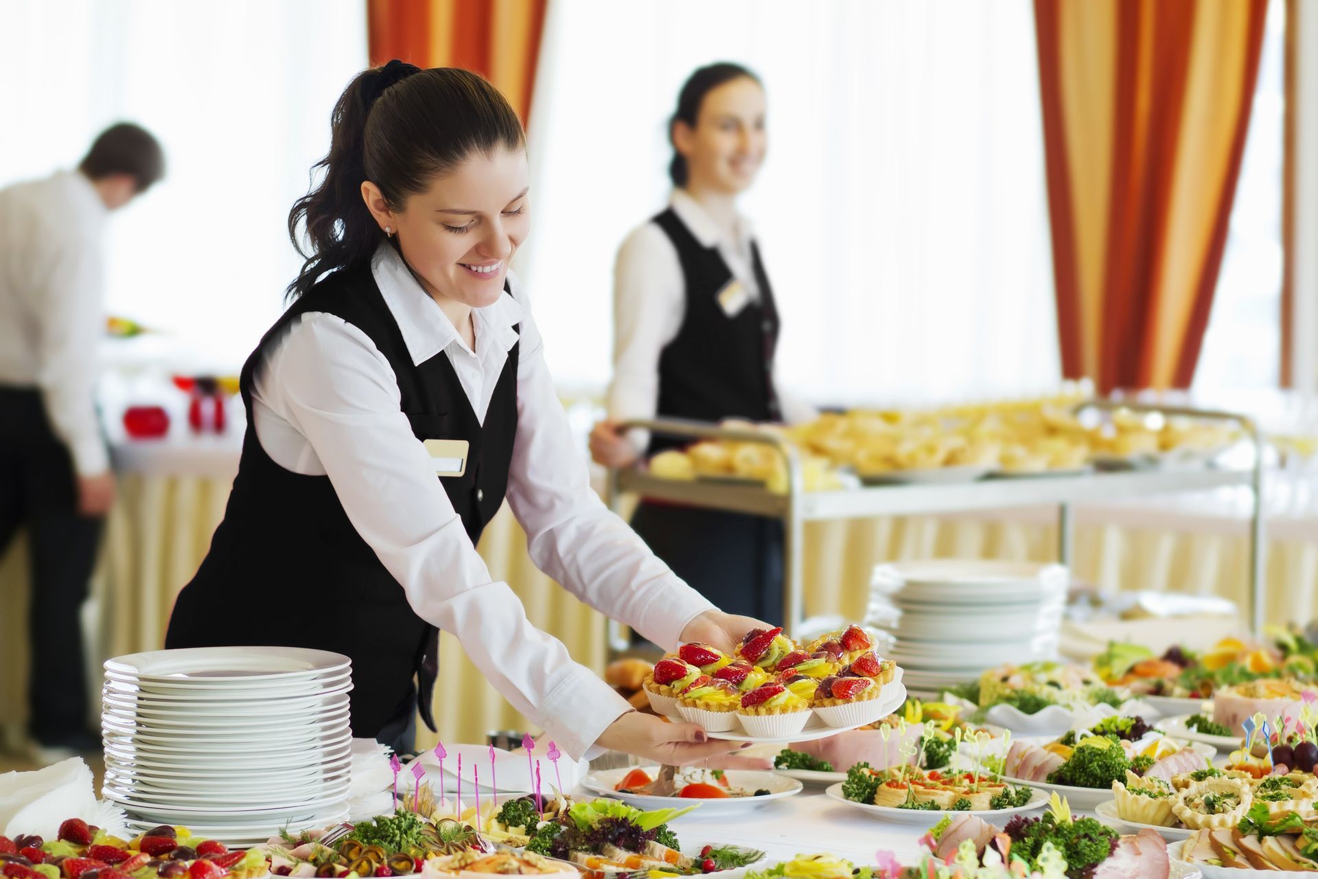 A woman is setting fruit tarts at an event.