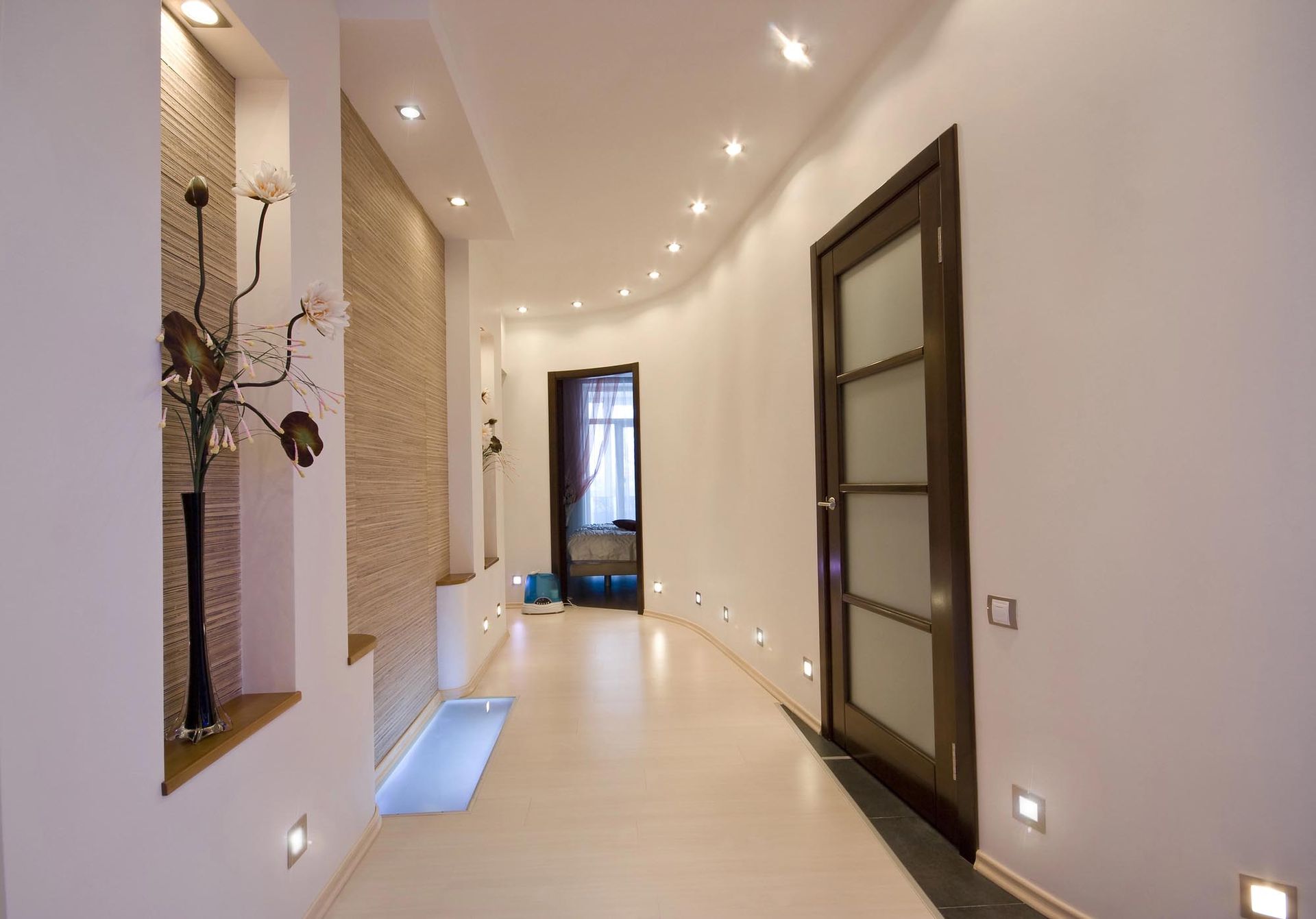 Corridoio con illuminazione da incasso, parete beige e porta marrone scuro.