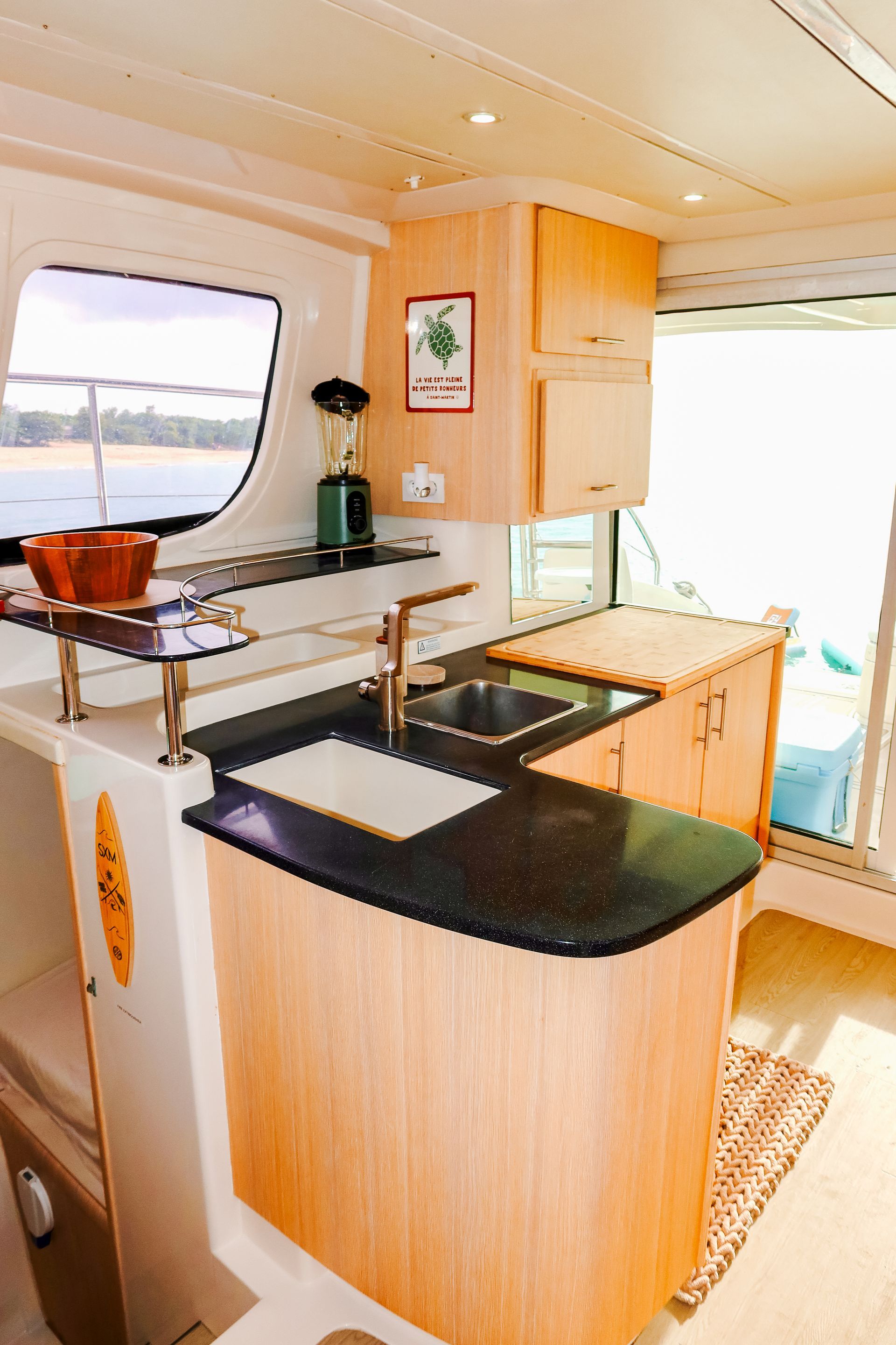 A boat kitchen with light wood cabinetry, granite countertop, sink, and window overlooking water.