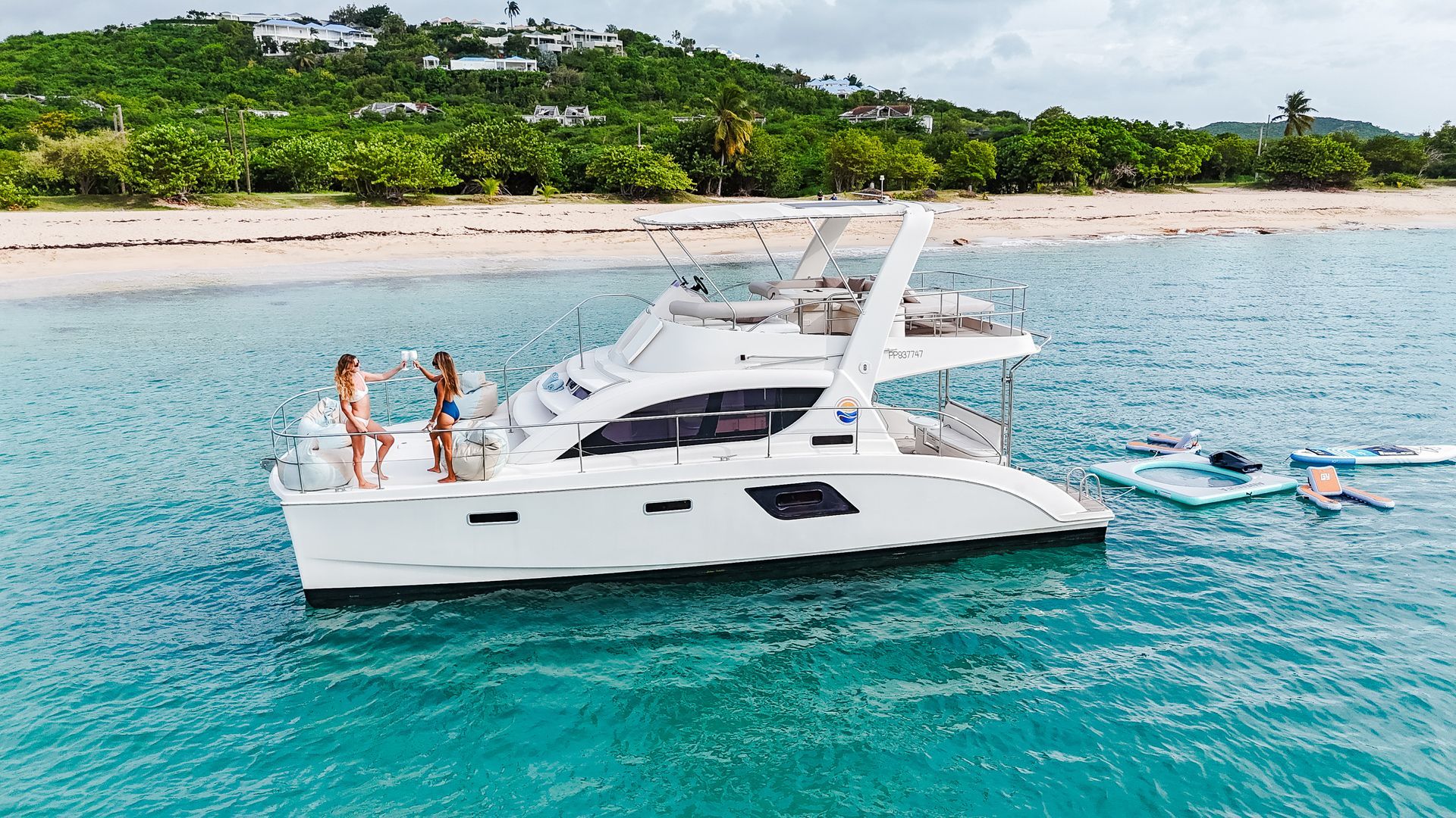 White catamaran on turquoise water with two people, beach, and green trees.