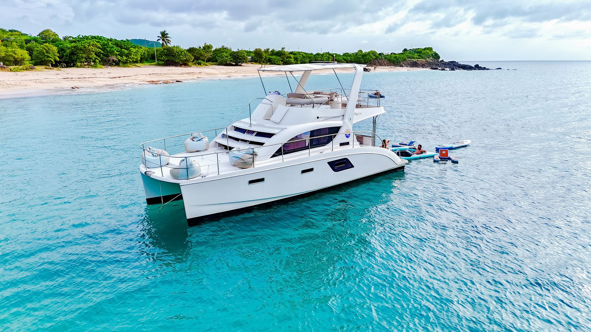 White catamaran docked in turquoise water near a sandy beach.