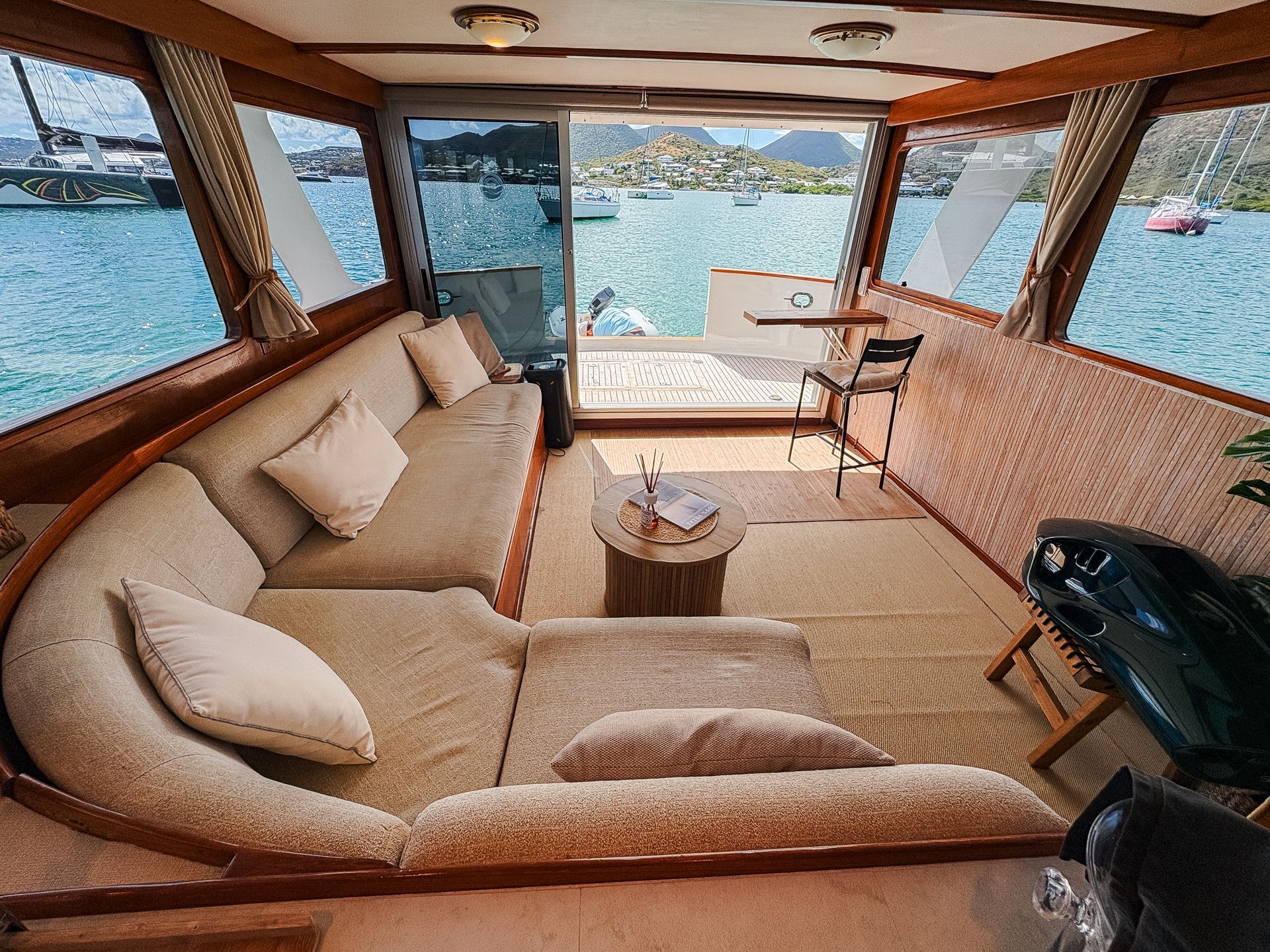 Interior of a boat cabin with wraparound seating, windows showing ocean views, and a small table.