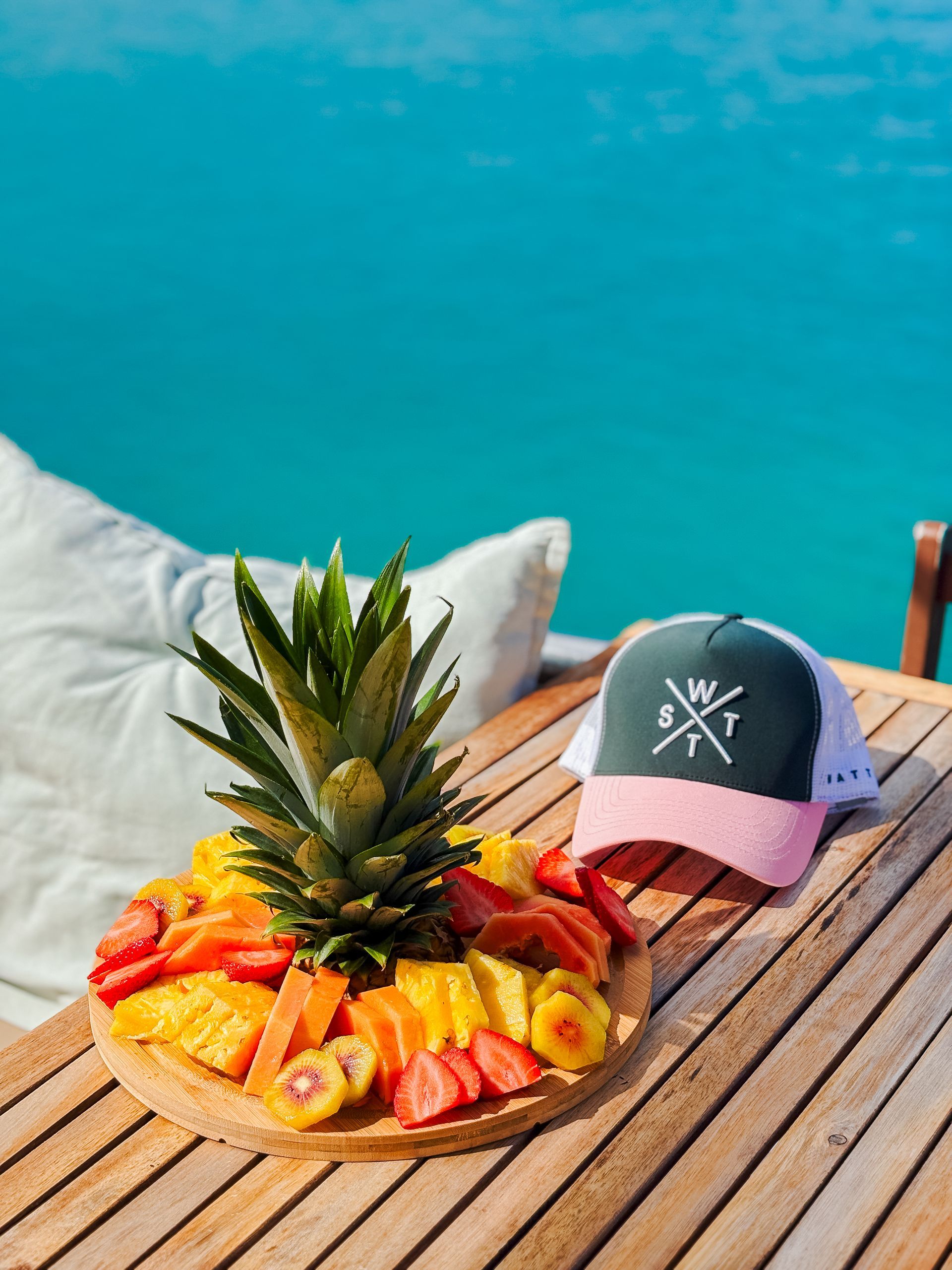 Fruit platter and cap on a wooden table, ocean in the background.