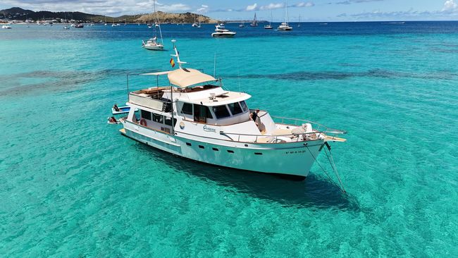 White yacht floating in turquoise water near a sandy beach under a blue sky.