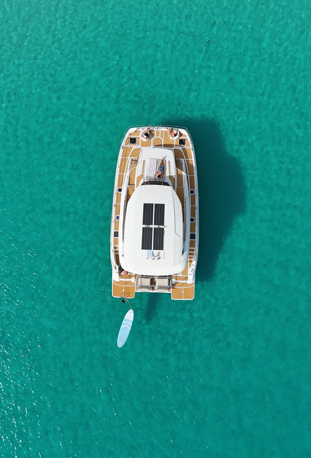 White yacht floats in turquoise water with a bright blue sky, near a beach and hillside.
