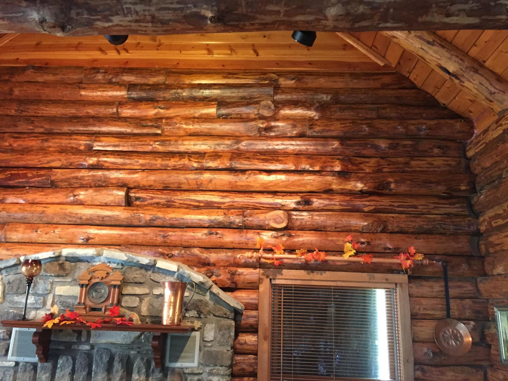 Wooden log cabin interior with logs, stone fireplace, and a window with blinds.