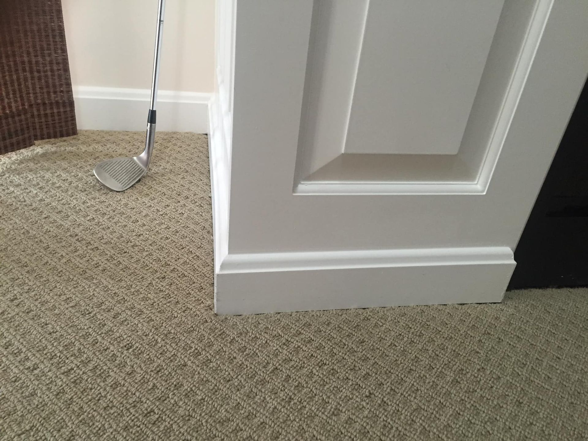White-trimmed door baseboard on patterned carpet. A golf club rests against the wall.