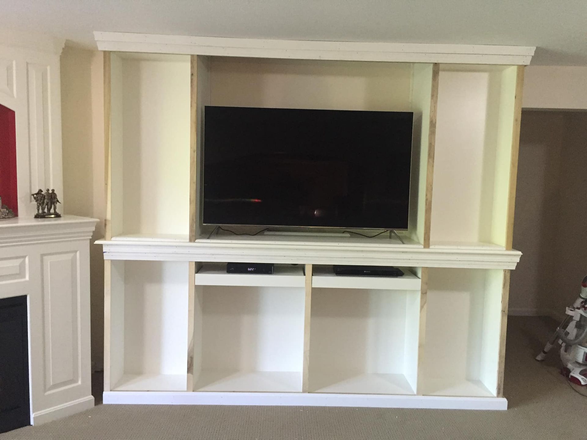 White built-in entertainment center with a large TV, storage shelves, and space for media players.