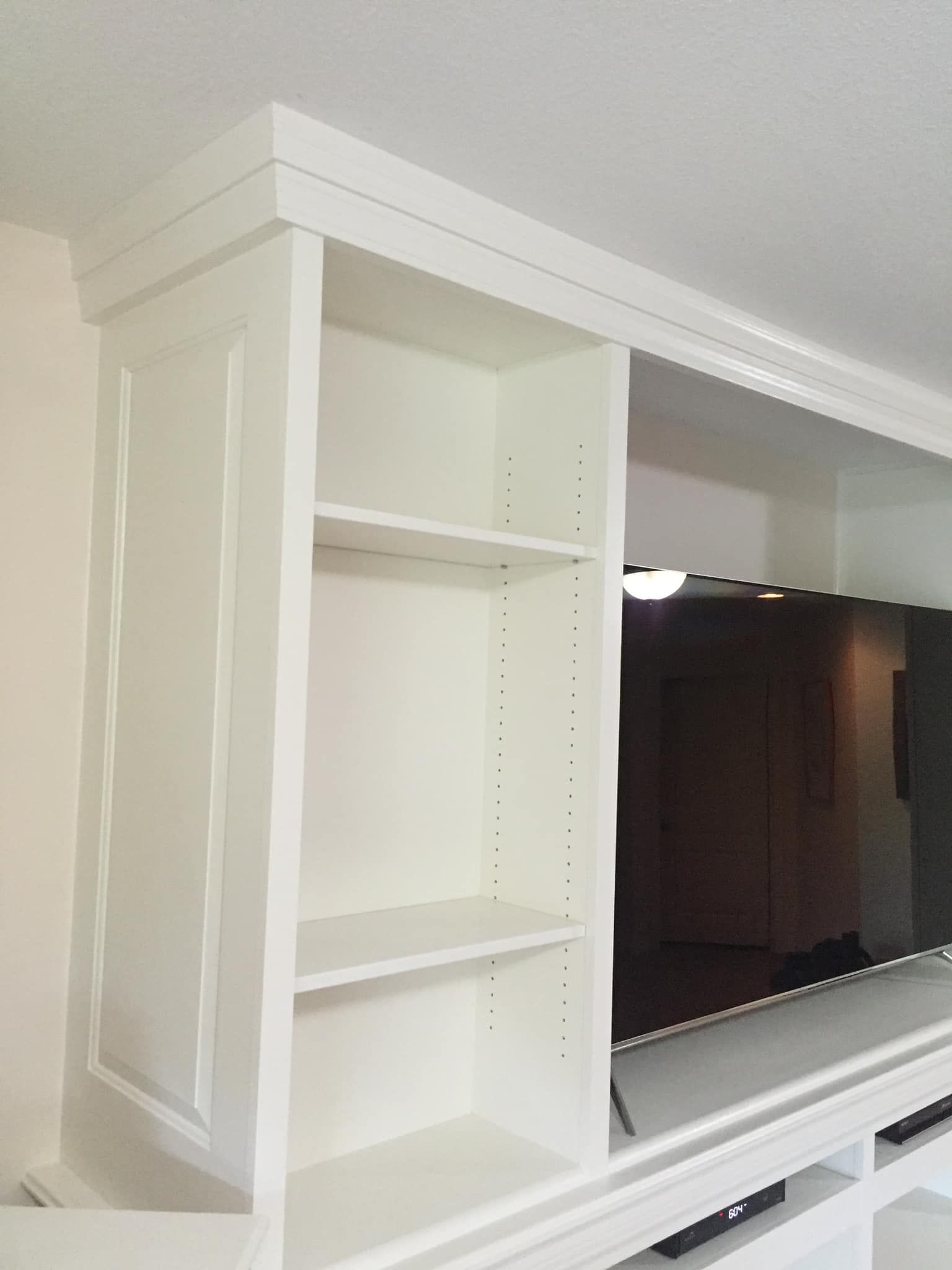 White built-in cabinet with open shelves next to a flat-screen TV, installed on a white wall.
