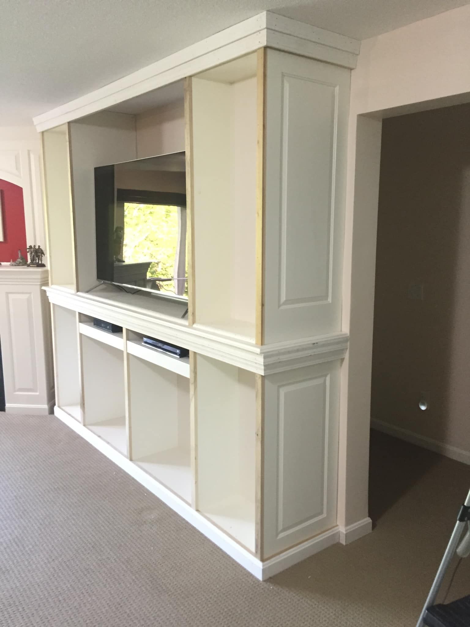 White built-in entertainment center with a TV, shelves, and storage cabinets in a living room setting.