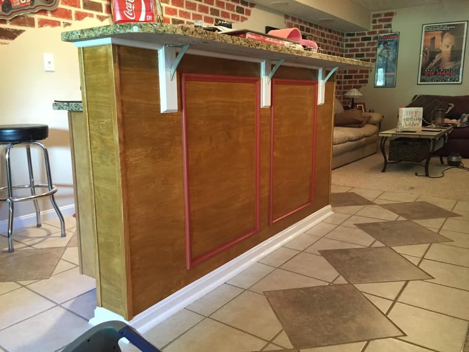 A wooden home bar with a granite countertop, white brackets, and tiled floor.
