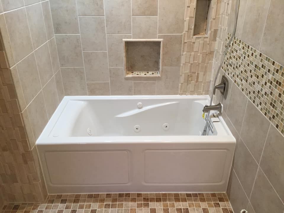 White bathtub with tile surround and mosaic accents.
