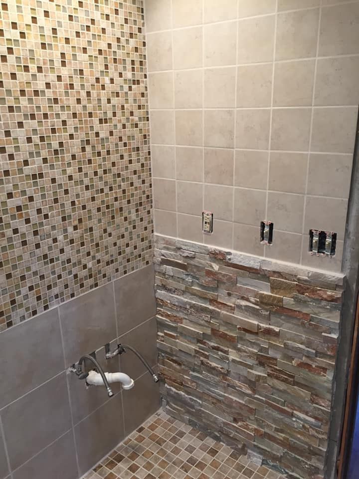 Bathroom with tiled walls and floor, featuring mosaic, stone, and beige tiles.
