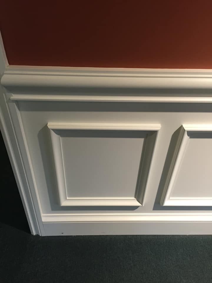 White paneled wall with decorative molding against a red wall and gray carpet.