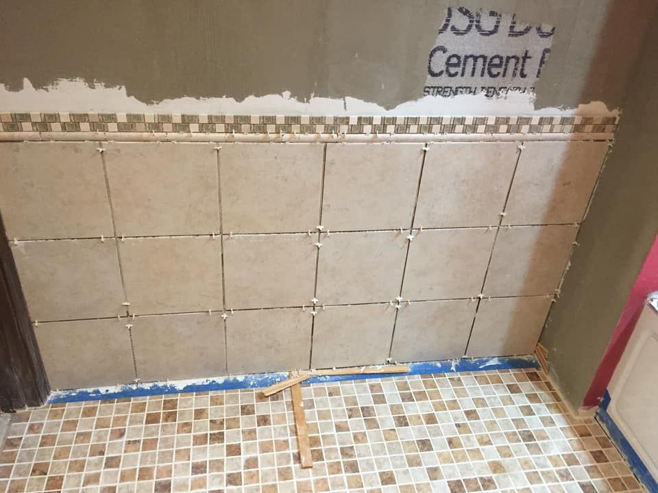 Bathroom wall tiling in progress; tan tiles with spacers, a decorative border, and cement board visible.