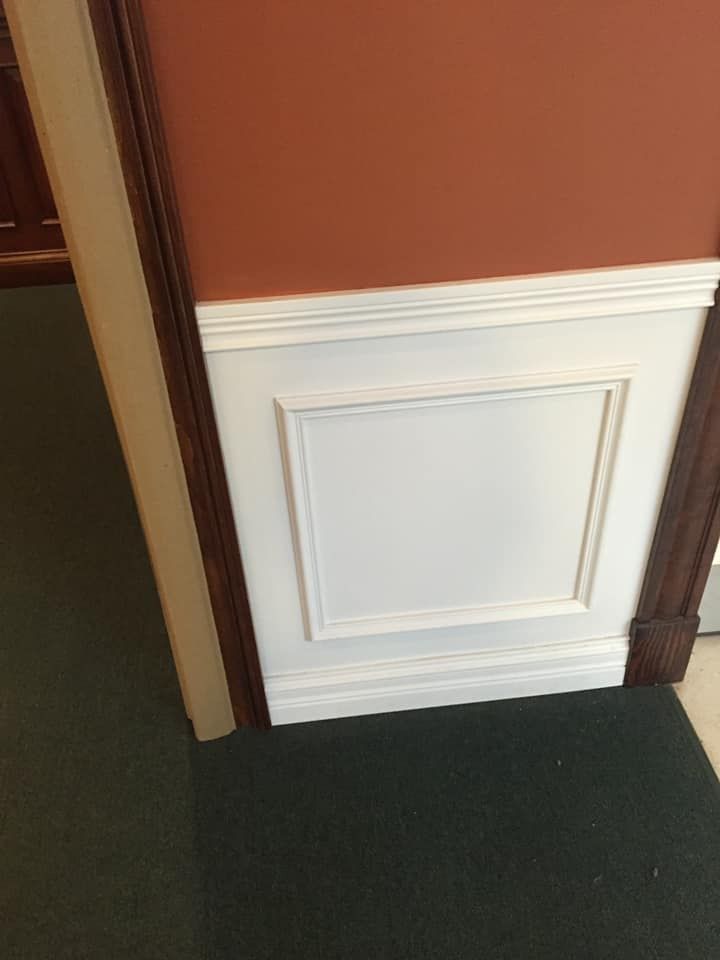 White wall paneling with brown trim, against a rust-colored wall.