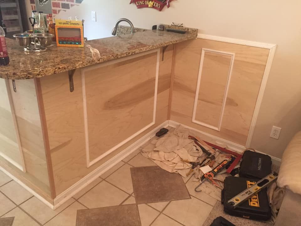 Interior shot of a bar under construction, featuring wood paneling with white trim, countertop, tools on the floor.