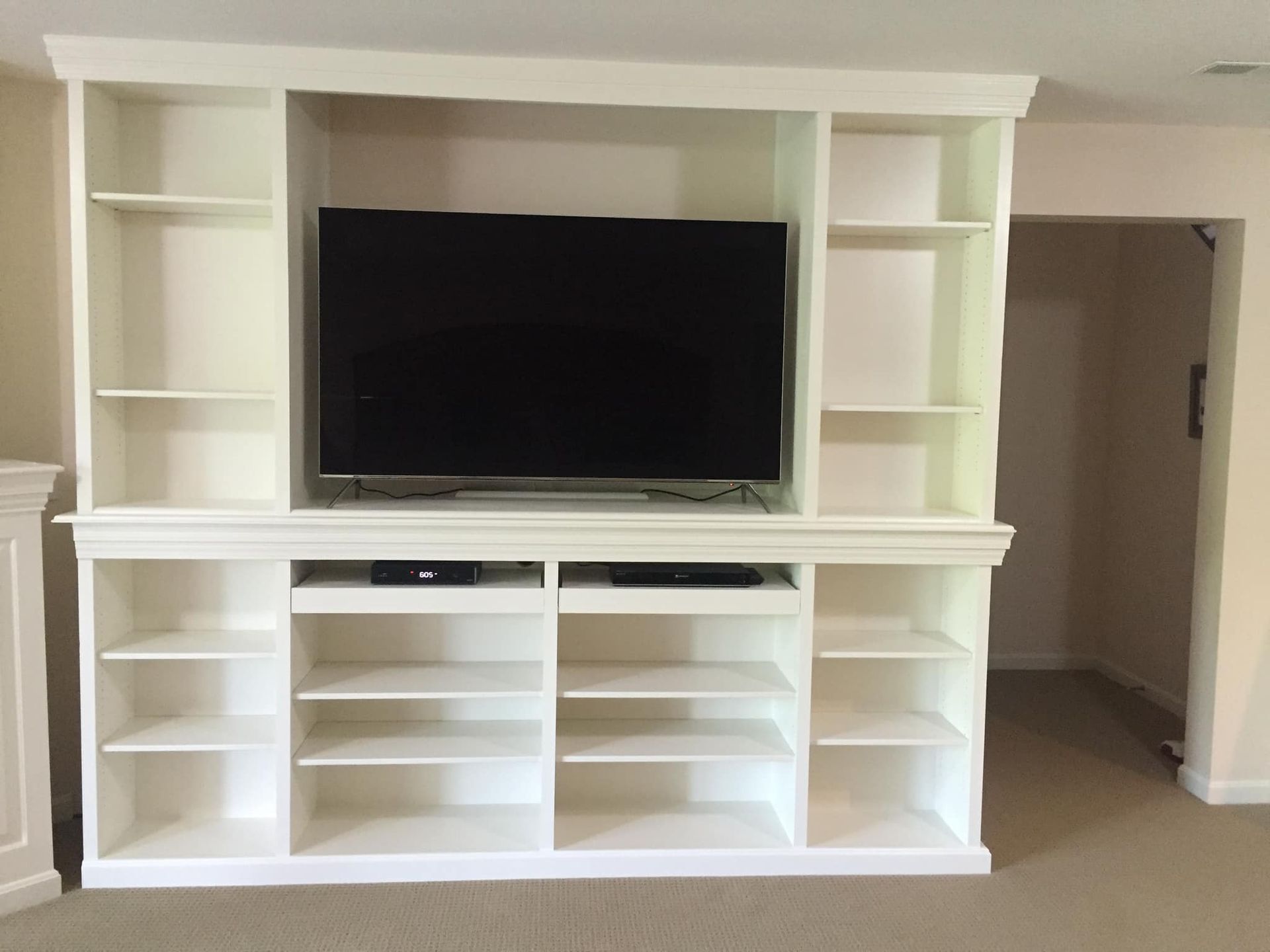White built-in entertainment center with television, shelves, and storage in a room.