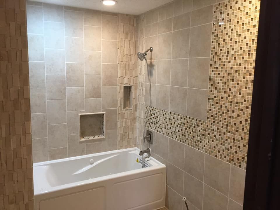 Bathroom with a white bathtub, tiled walls in beige and mosaic, and a showerhead.