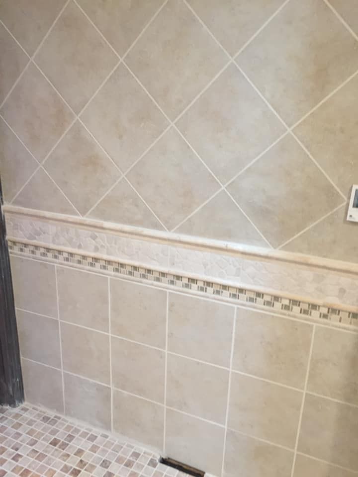 Tiled shower wall with diagonal and square beige tiles, mosaic border, and floor.