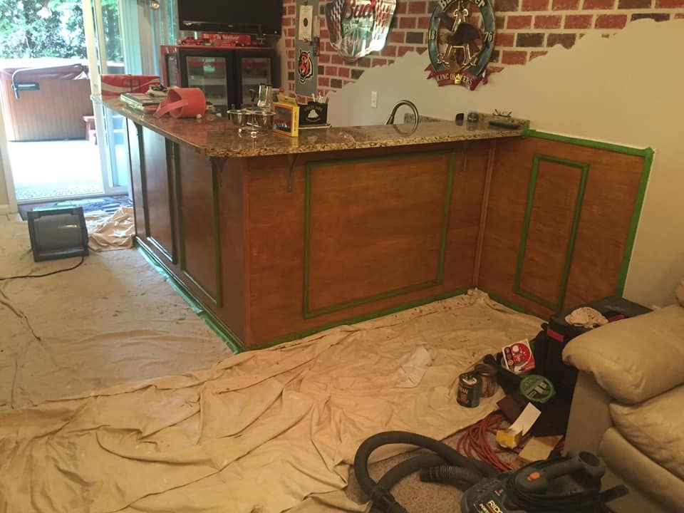 Bar with wood paneling and green trim, undergoing renovation. Beige paint cloths cover the floor.
