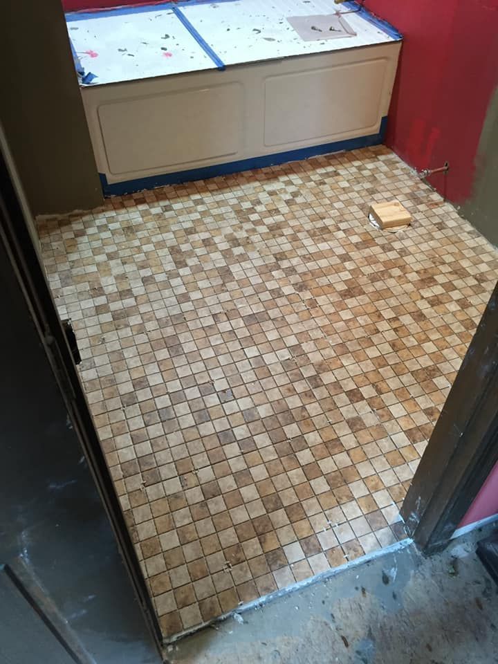 Bathroom floor tiled with small beige and brown squares. A built-in white cabinet sits on the back wall.