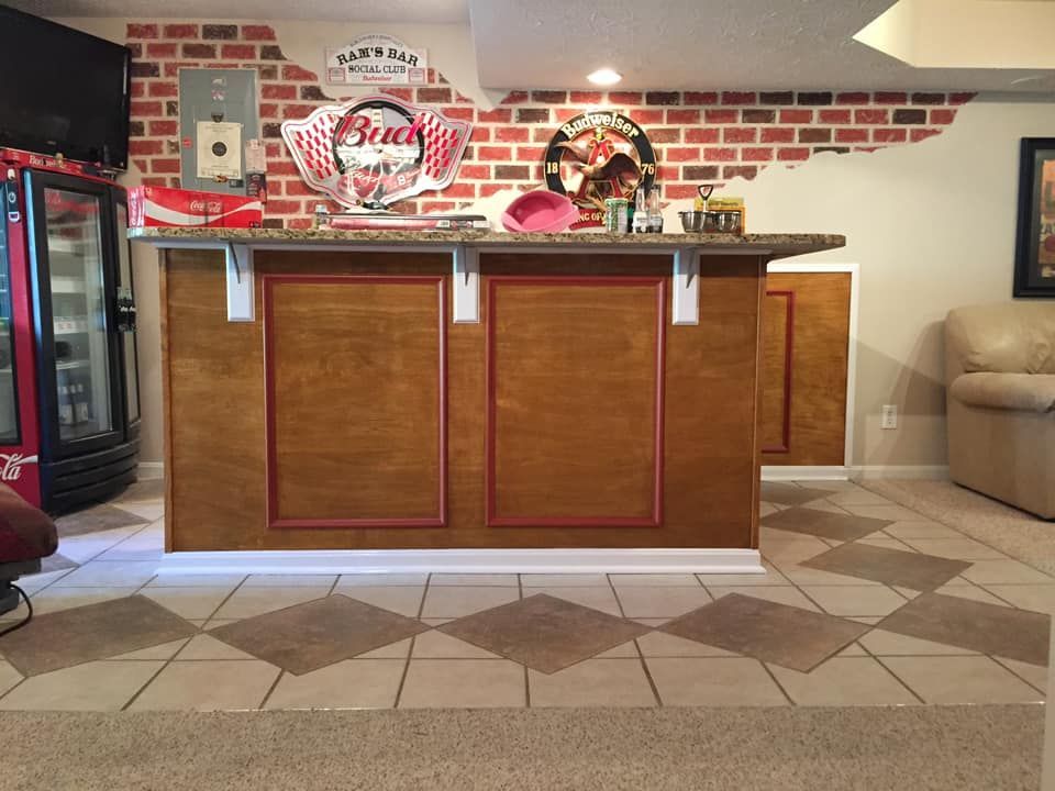 Bar with brown wood paneling and a granite countertop, in front of a brick wall, with a Coca-Cola vending machine.