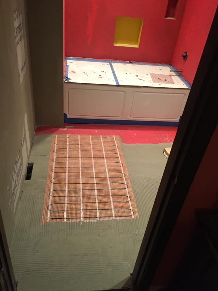 Bathroom remodel in progress: heated floor mat laid on green tile, bathtub, and red walls.