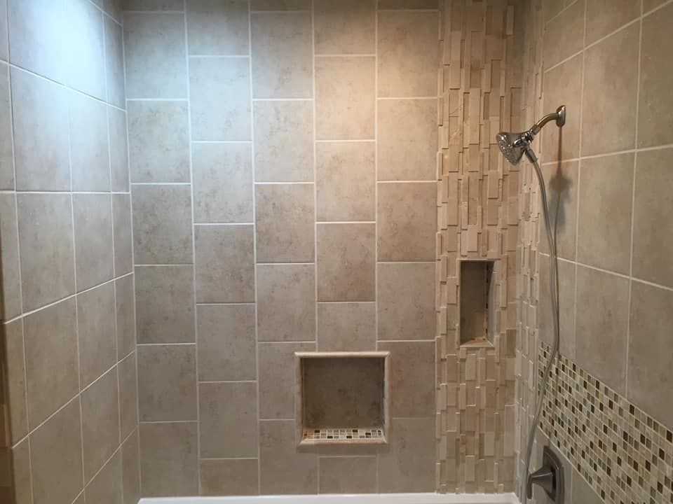 Tiled shower with beige and brown tiles. Includes a recessed shelf and showerhead.