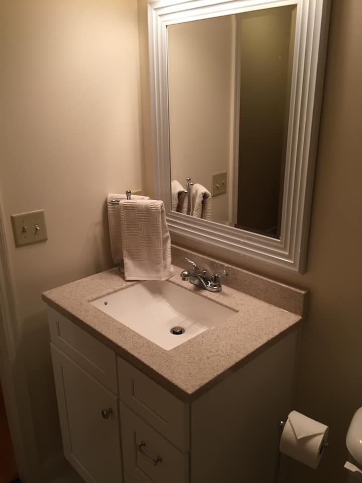 Small bathroom with a white vanity, sink, and mirror. White towels rest on the countertop.