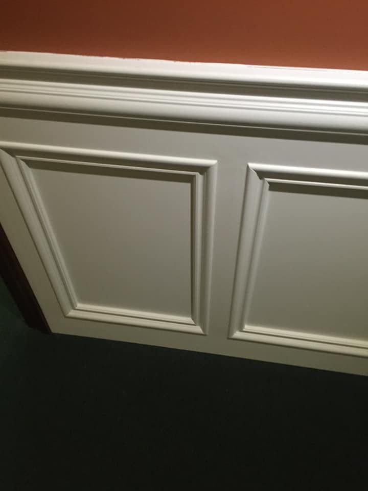 White paneled wall trim below an orange wall, casting a shadow on a dark blue wall.