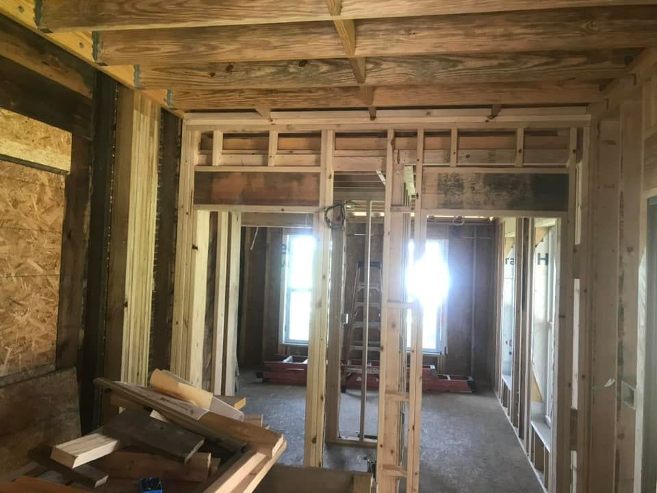 Interior view of a building under construction, featuring wooden framing, doorways, and natural light from windows.