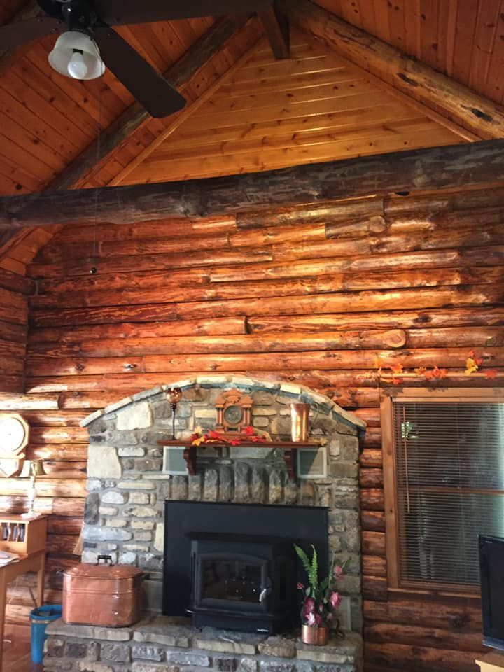 Log cabin interior with stone fireplace, wooden walls and ceiling, window.