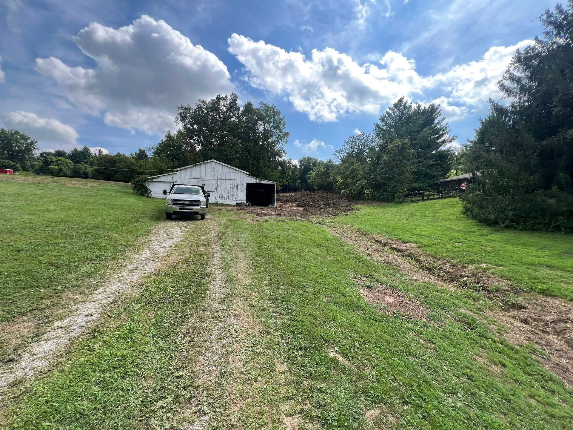 Gravel driveway leads to a white barn with a truck parked in front; green grass surrounds.