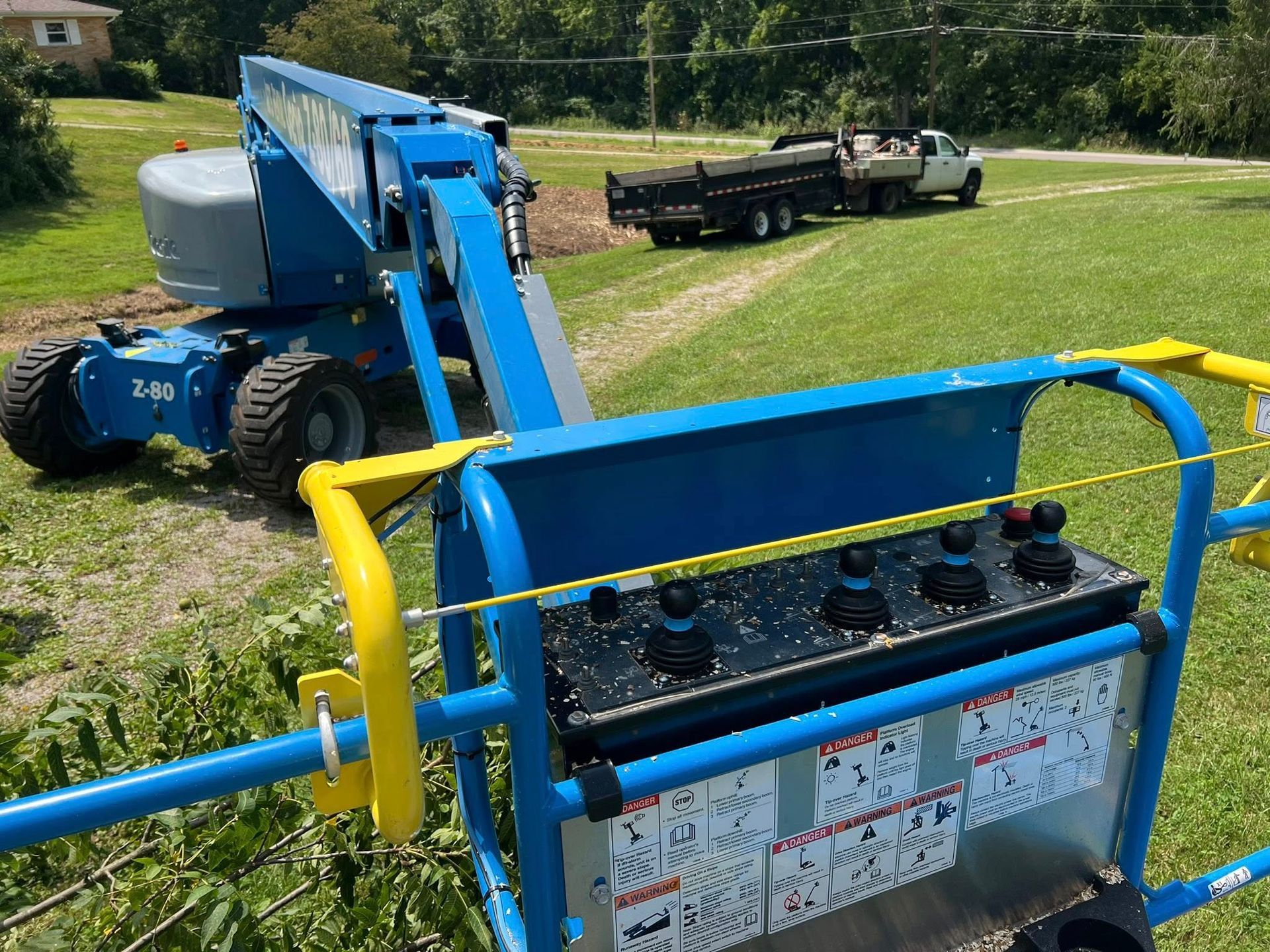 Blue aerial lift on green grass, with a truck in the background, controls in focus.