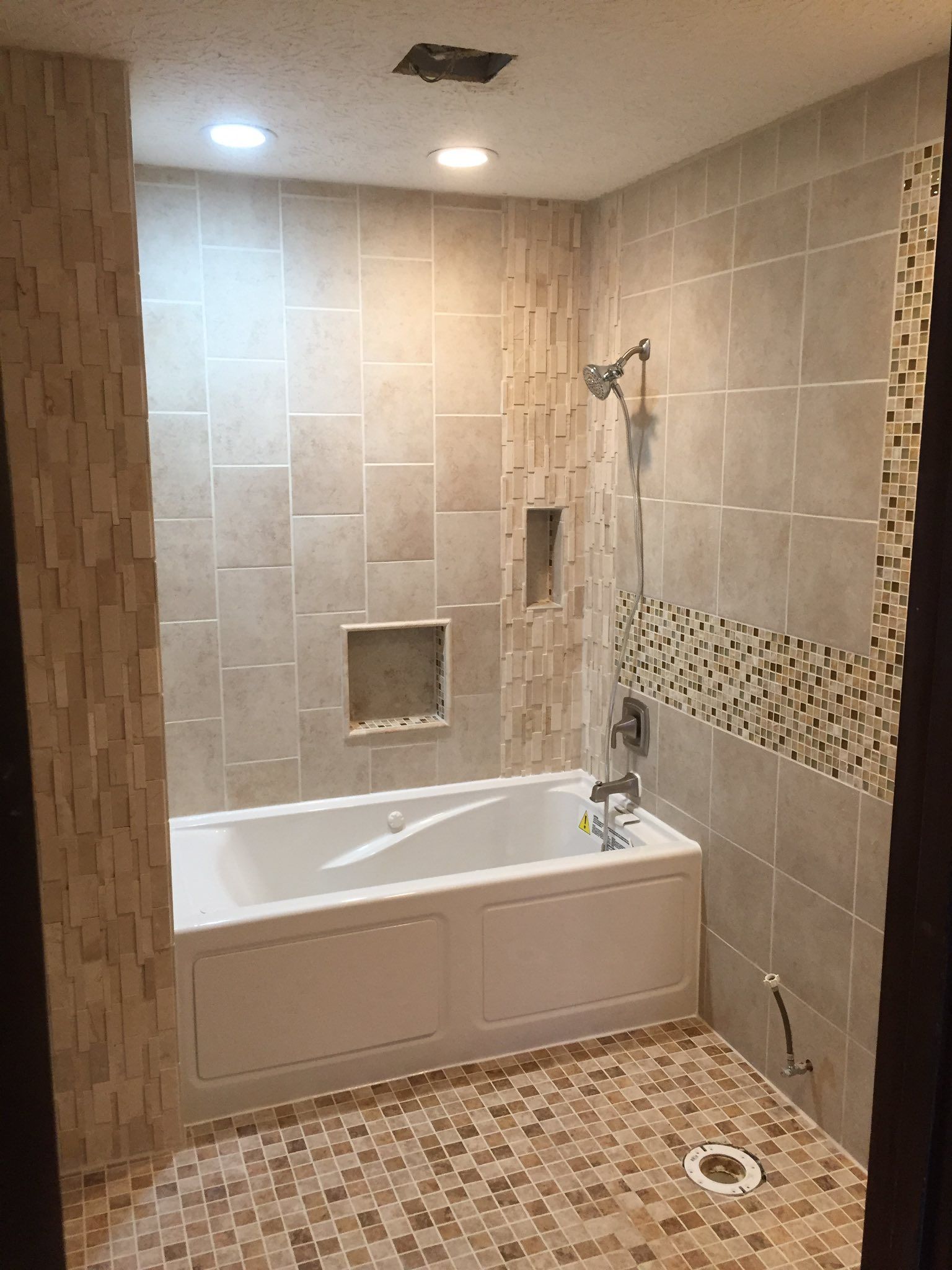 Tiled bathroom with a bathtub, showerhead, and mosaic tile accents.