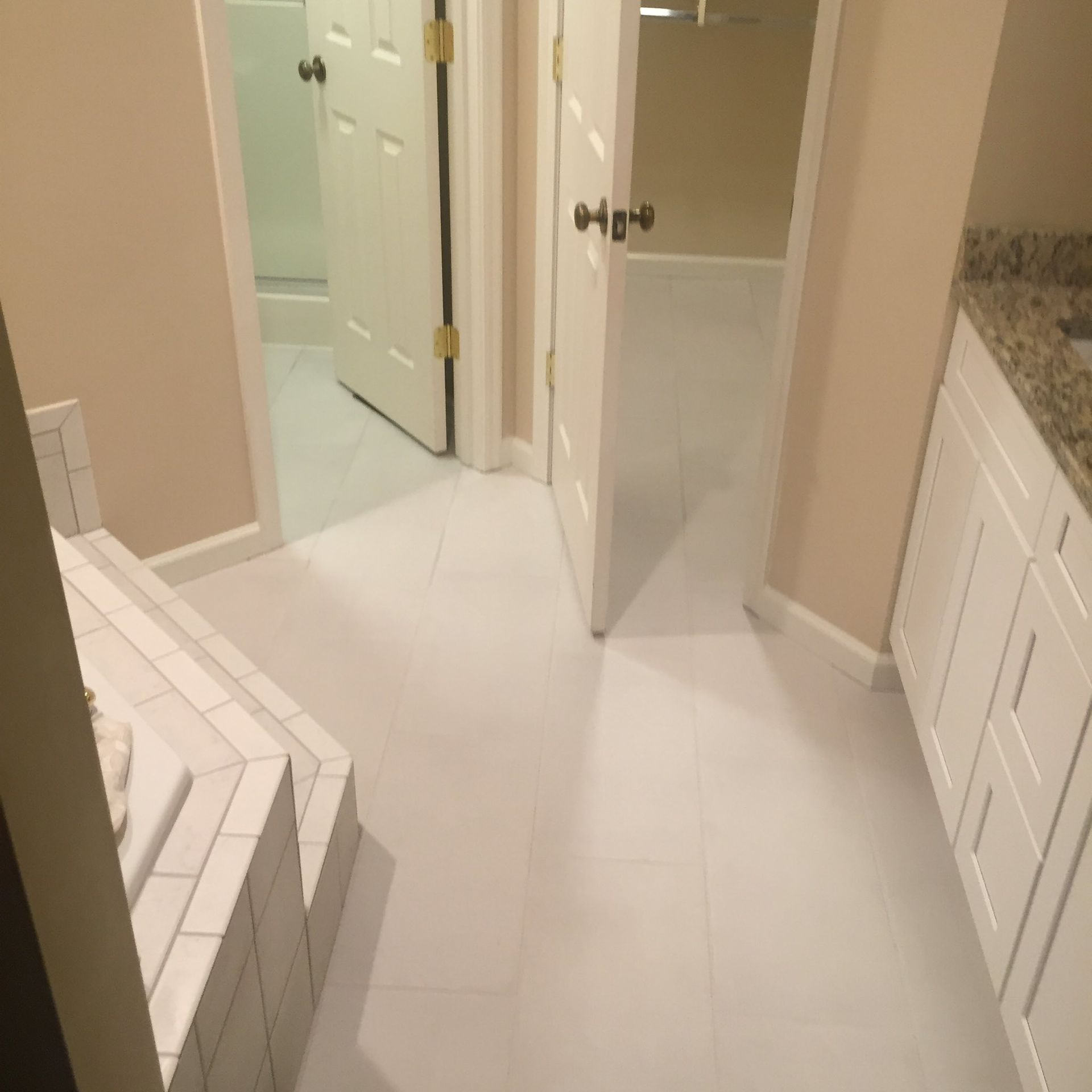Bathroom with white tile floor, white cabinets, and beige walls. Open doorways lead to other rooms.