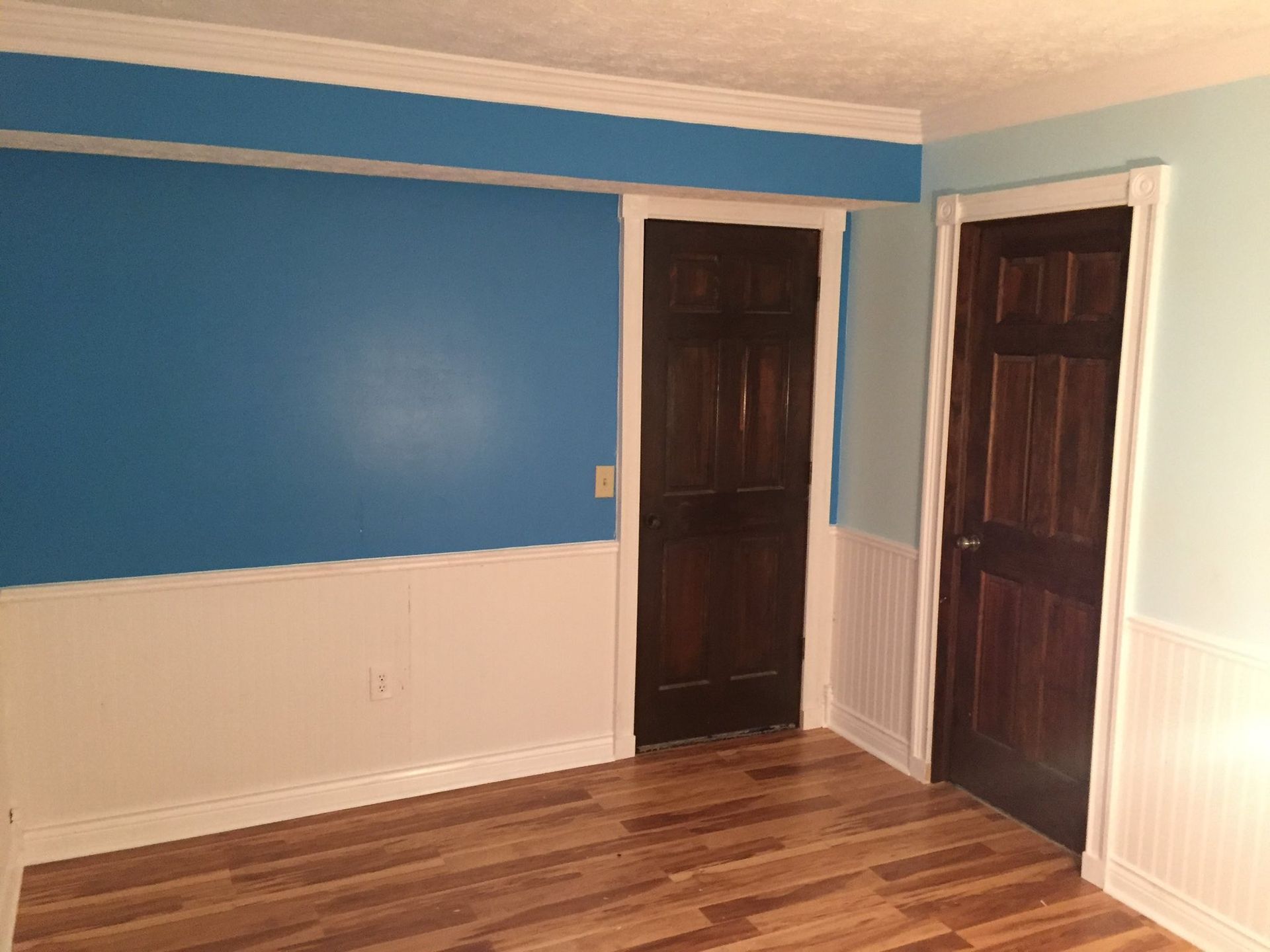 Room with blue and white walls, two brown doors, and wood-look flooring.