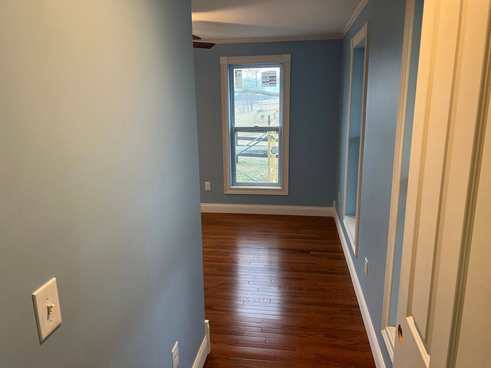 Narrow hallway with wood floors, blue walls, and a window at the end.