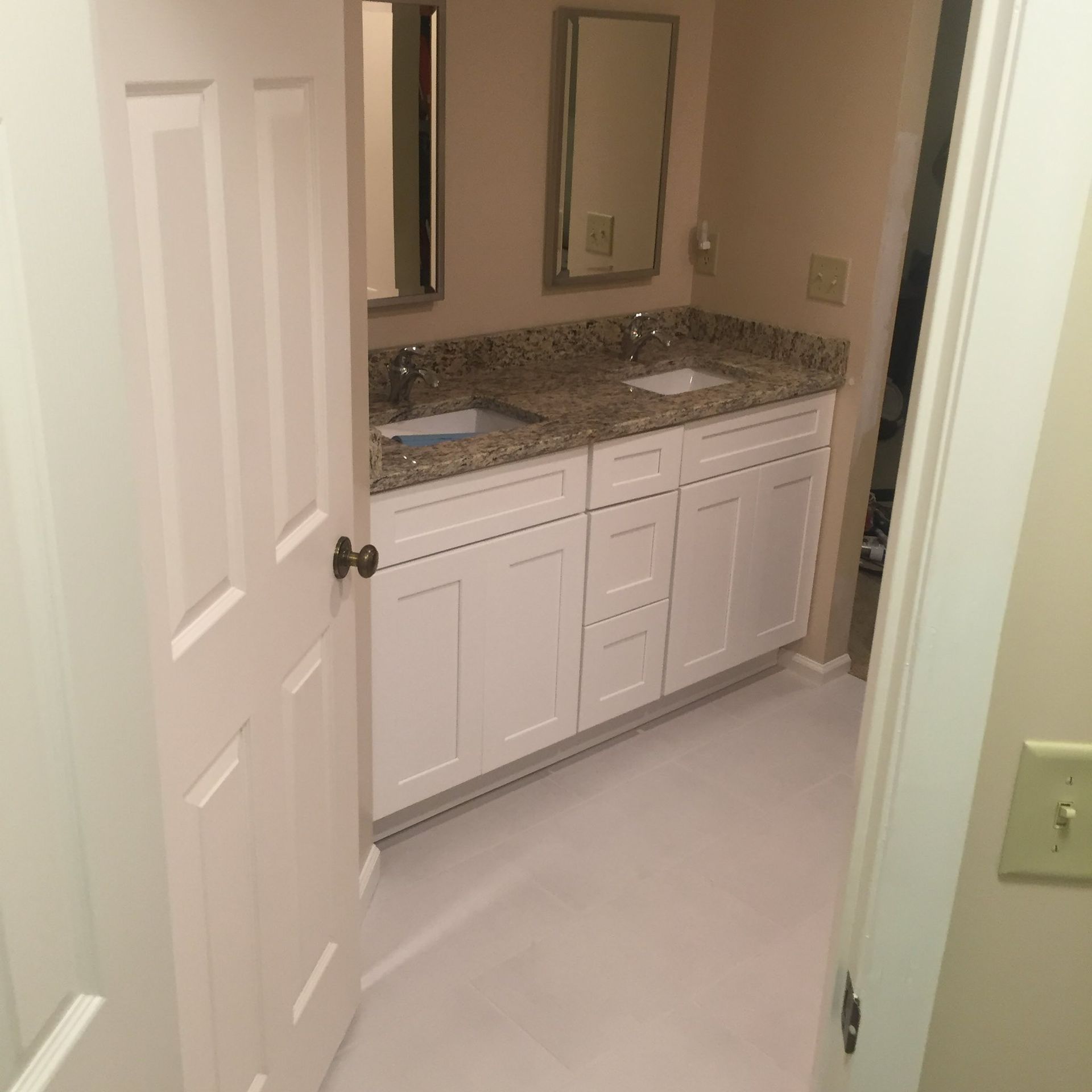 White bathroom with double vanity, granite countertop, two mirrors, and a closed door.