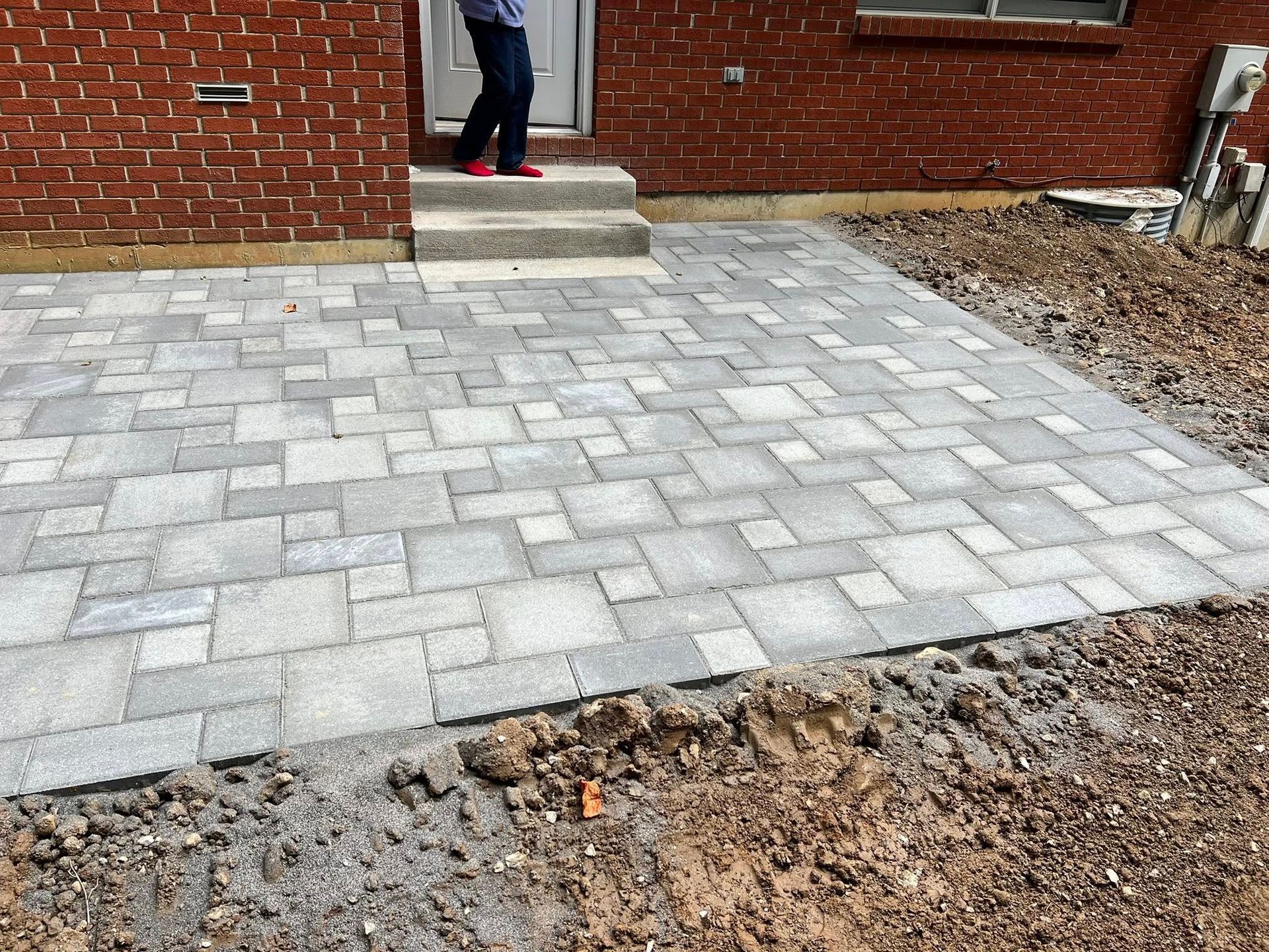 Newly constructed gray stone patio adjacent to a brick house and doorway; person standing in the doorway.