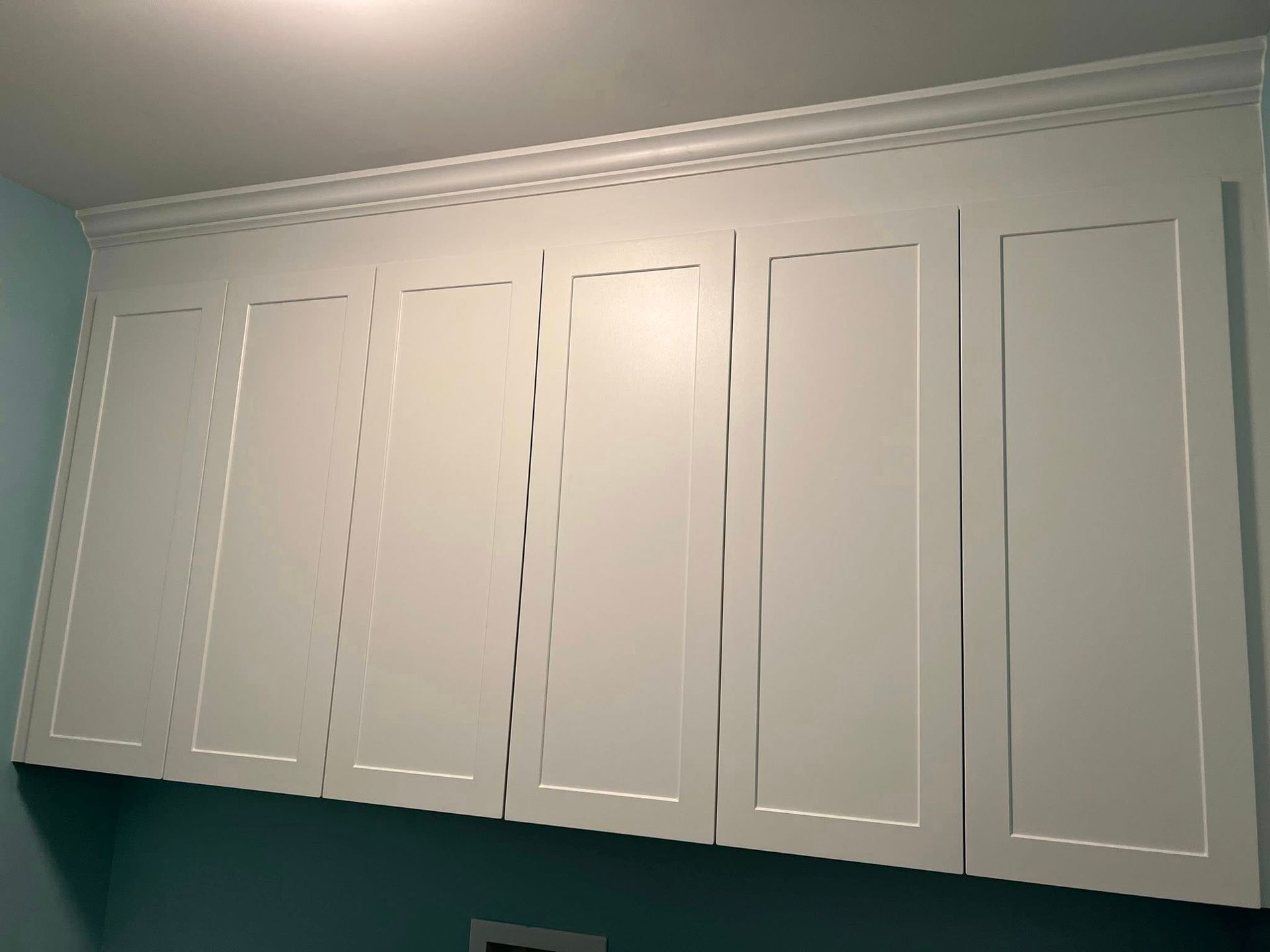 White overhead cabinets with crown molding against a light blue wall.