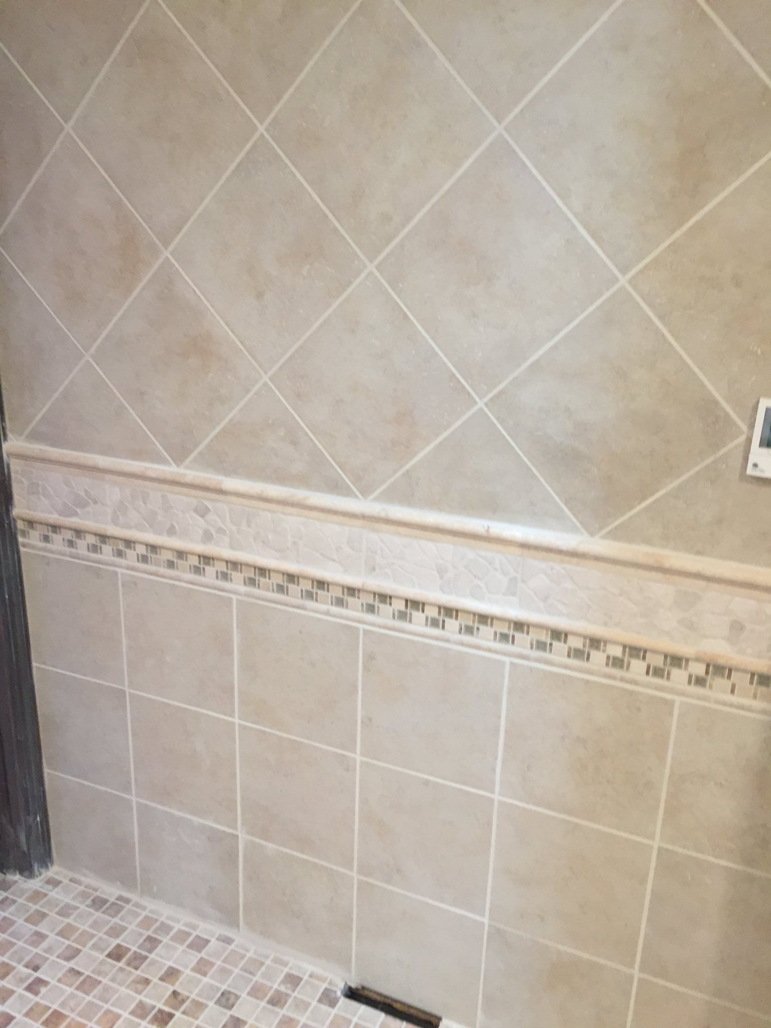 Beige tiled shower with diagonal and square patterns, decorative border, and a small mosaic floor.
