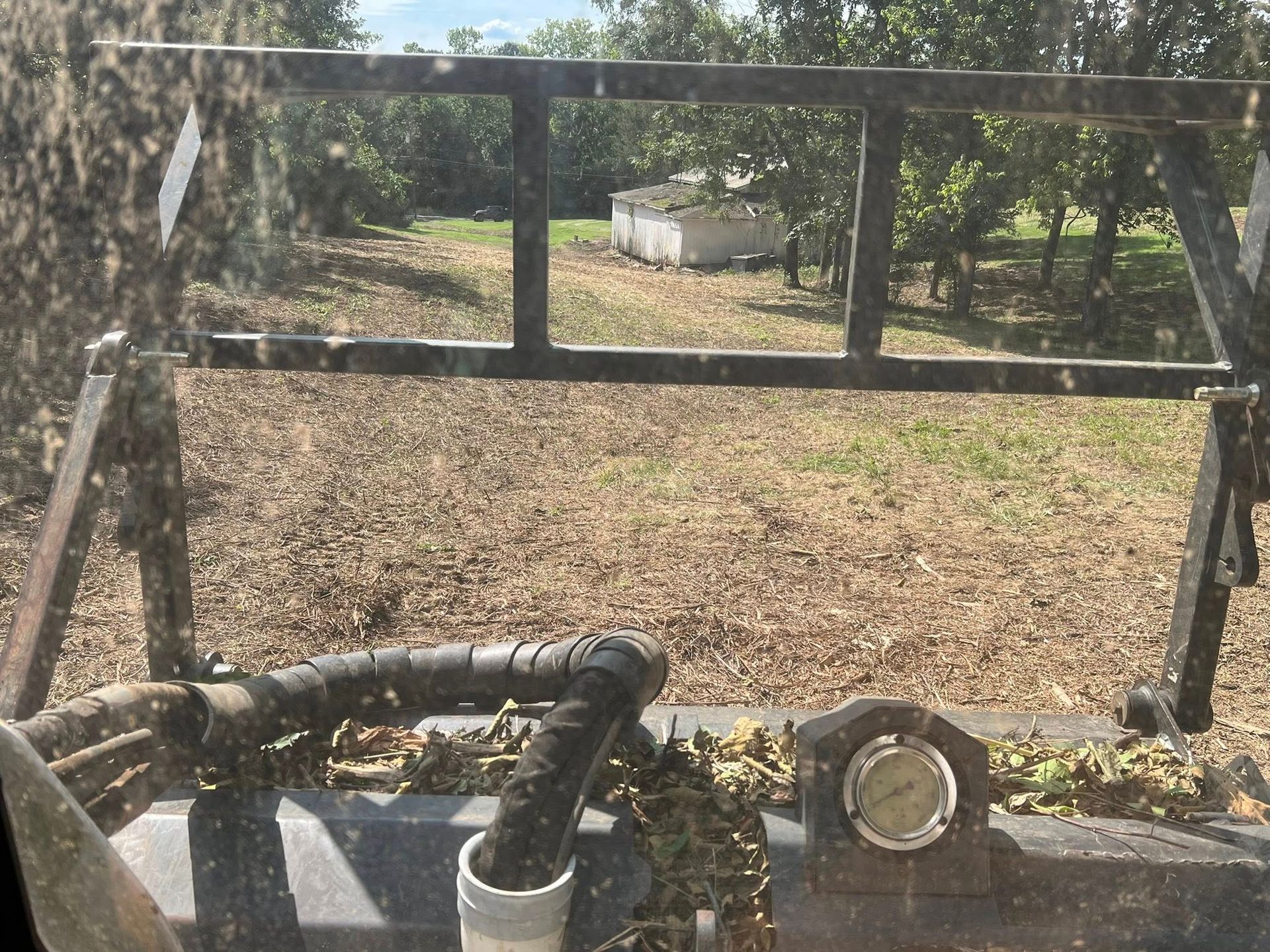 View from a tractor cab, across a field to a building and trees.