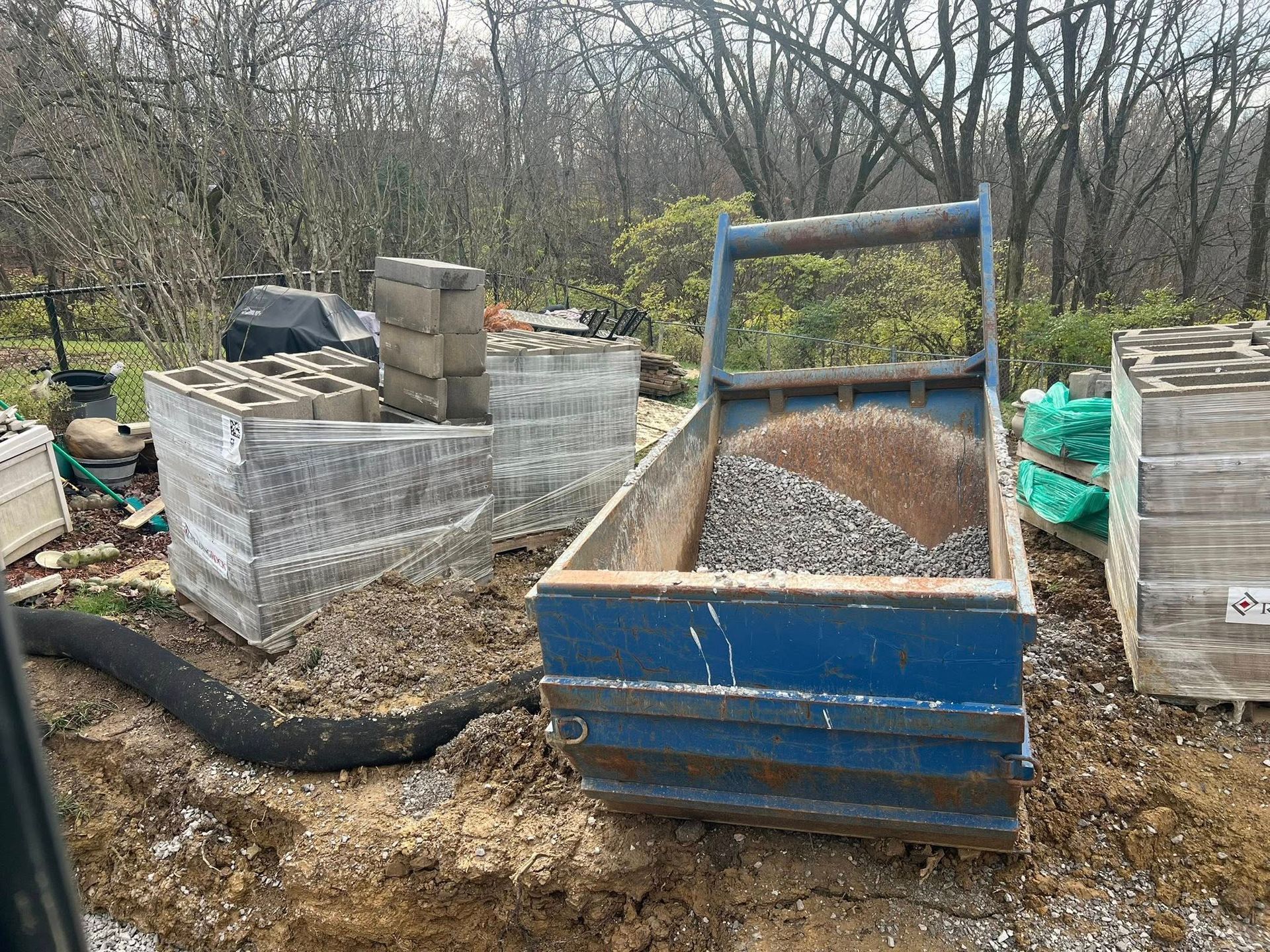 Blue dump cart with gravel, surrounded by paving stones and construction materials.