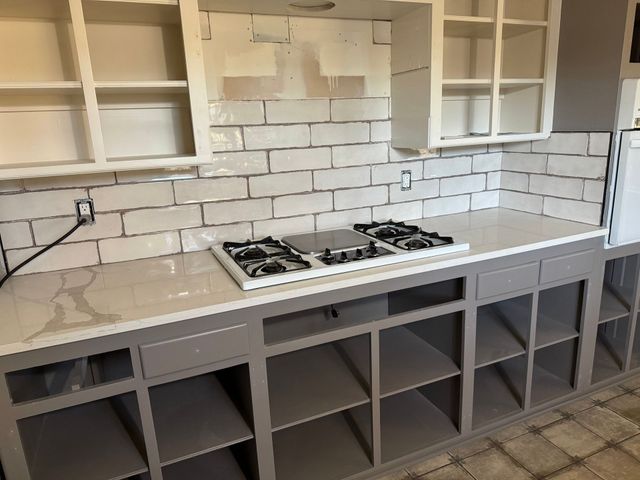 Modern kitchen with gray cabinets, white subway tile backsplash, and a gas cooktop under open shelves