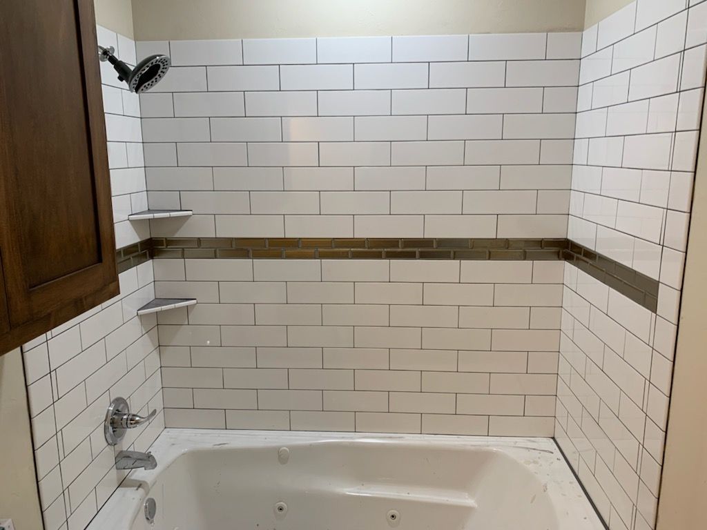 Small tiled bathroom with a bathtub, white subway tiles, and a window above the tub.