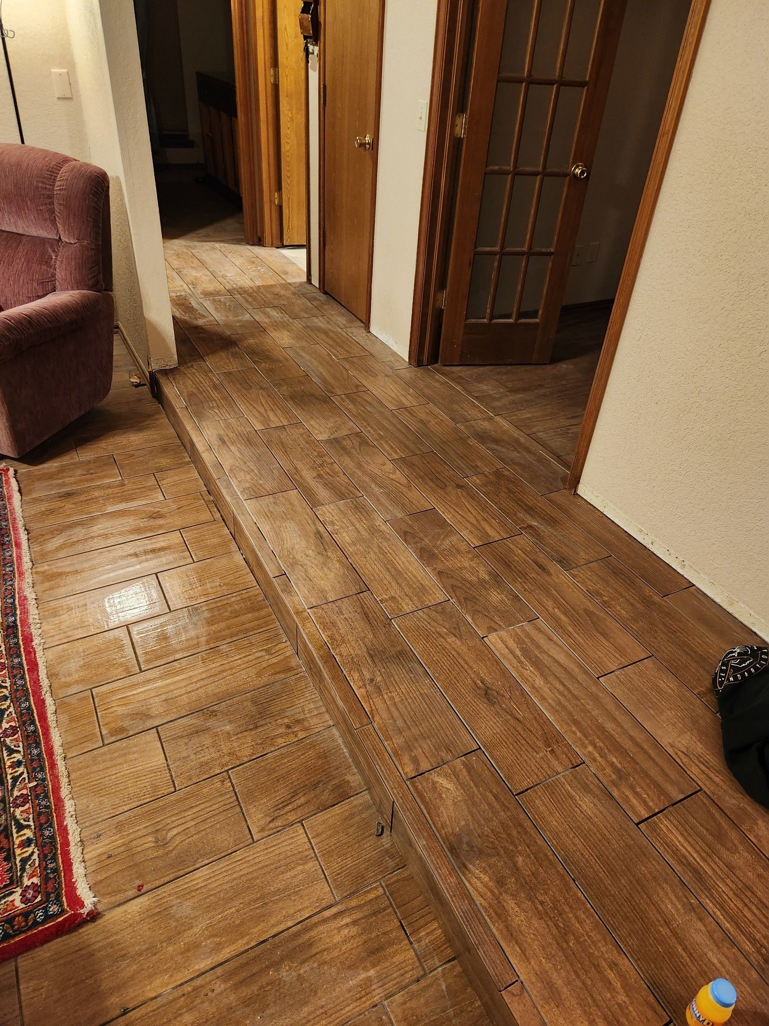 Wooden hallway floor with visible water damage, leading past open doorways in a home.