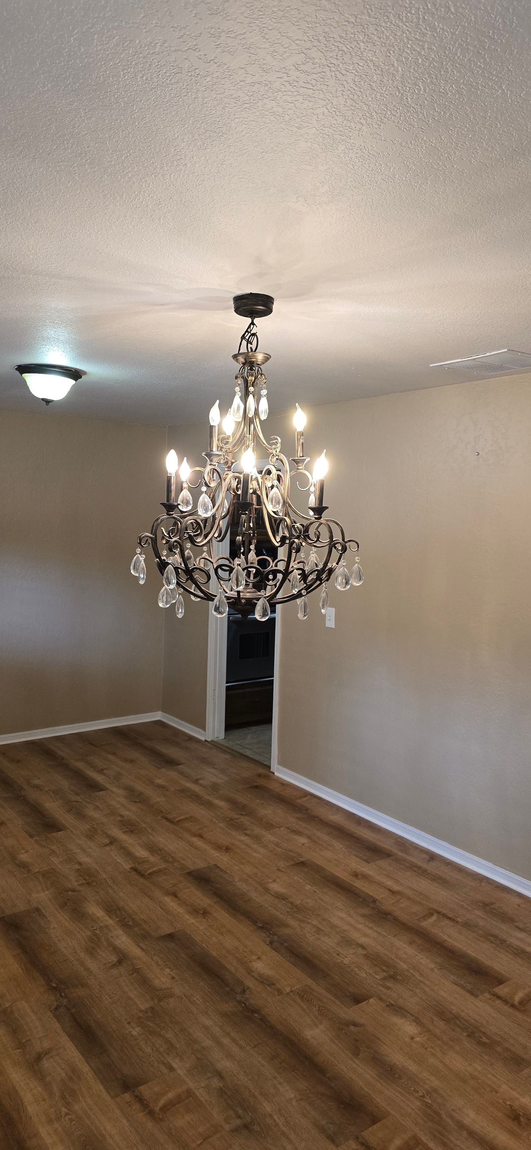 Empty room with wood floors, beige walls, and a decorative chandelier hanging from the ceiling.