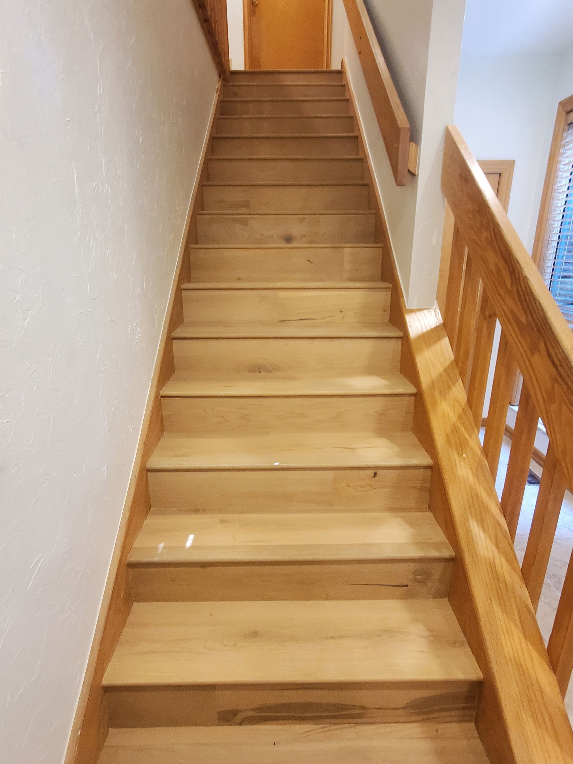 Wooden staircase with light walls and a railing, viewed from the bottom looking up